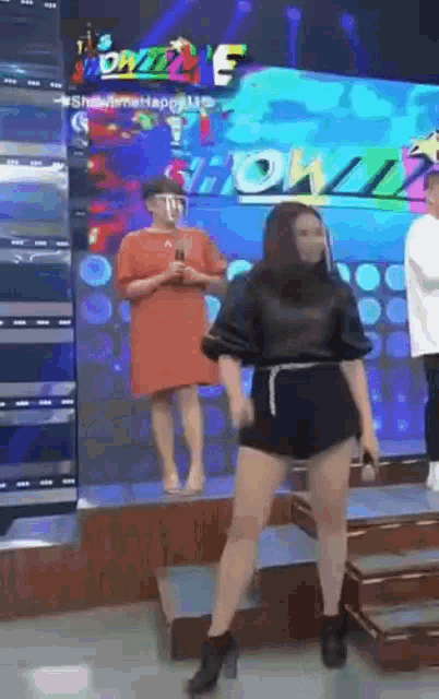 a woman in shorts is dancing on a stage in front of a sign that says showbiz