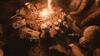 a group of people are sitting around a fire in the middle of a forest .