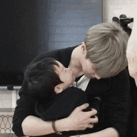 a man is kissing a little boy on the cheek while holding him in his arms .