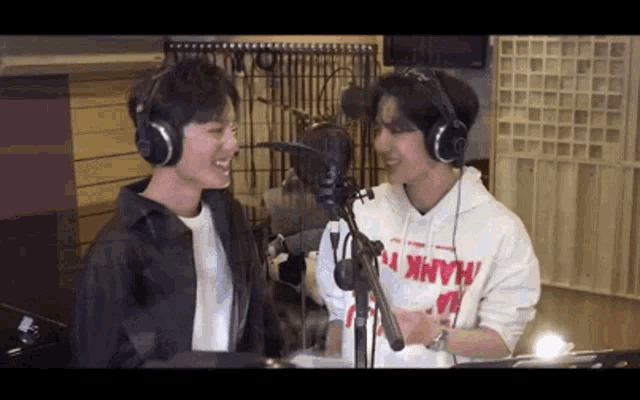 two men are standing next to each other in front of a microphone in a recording studio .