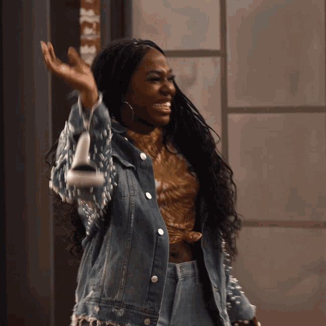 a woman wearing a denim jacket with pearls on the sleeves is waving