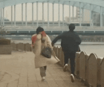 a man and a woman are running on a sidewalk holding hands .