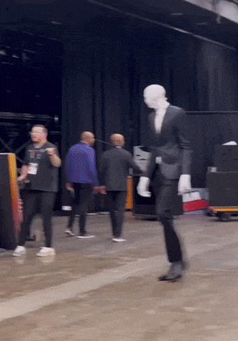 a man in a suit and white gloves is walking in a room with other people