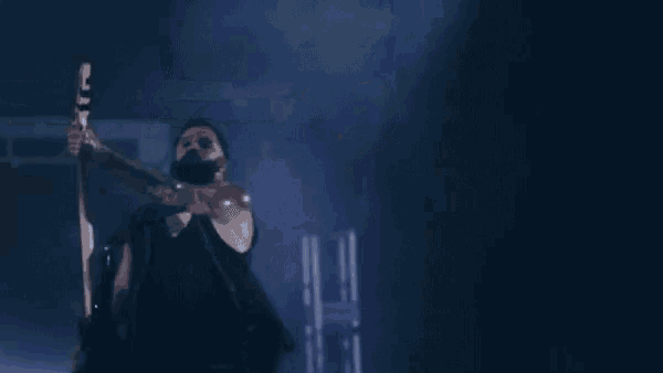 a man in a black tank top is playing a guitar in the dark