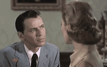 a man in a suit and tie is looking at a woman in a yellow shirt .