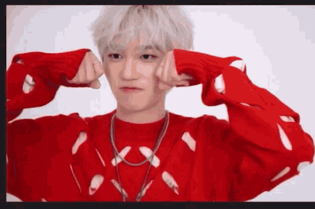 a man with white hair is wearing a red sweater and making a face