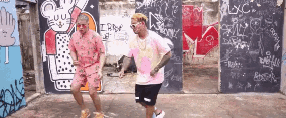 two men are dancing in front of a wall that has graffiti on it including the word lxc