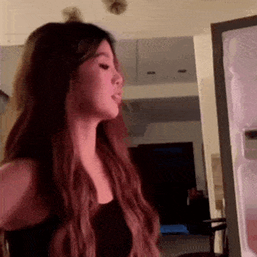 a woman with long brown hair is standing in front of a refrigerator .