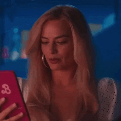 a woman is smiling while looking at a pink phone .