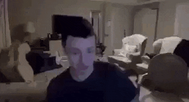 a man in a black shirt is sitting in a living room with a ghost behind him .