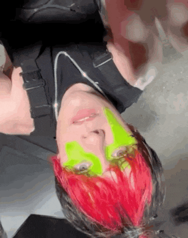 a person with red hair and green face paint is upside down .