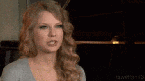 taylor swift is making a funny face while wearing a gray shirt .