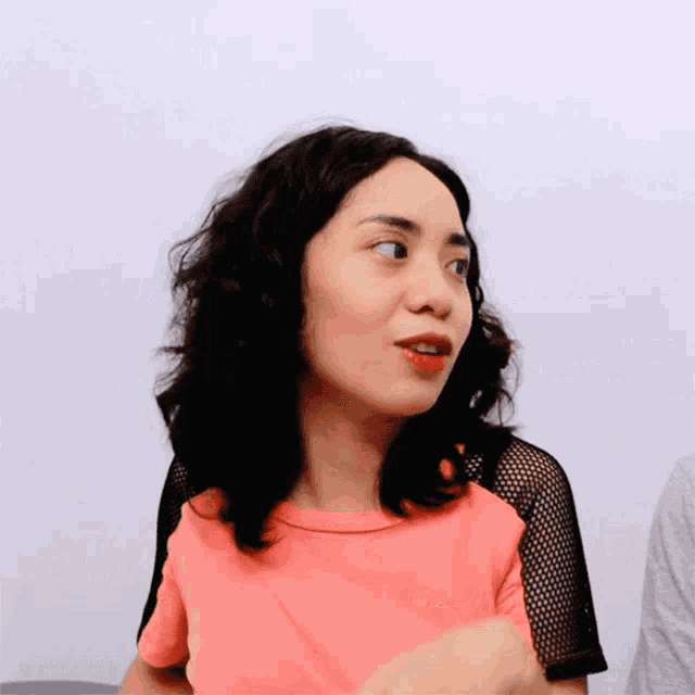 a woman wearing a pink shirt and black mesh sleeves looks at the camera
