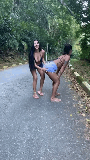 two women are standing on the side of a road one is holding the other 's butt