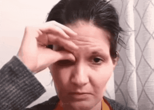 a woman wipes her forehead with her hand while wearing a sweater