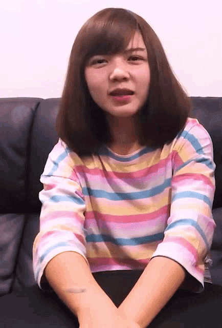 a girl wearing a colorful striped shirt is sitting on a couch