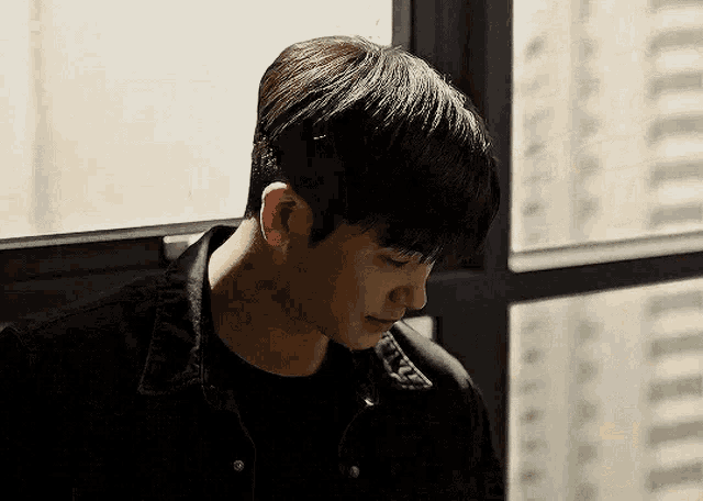 a young man is sitting in front of a window with his head down .