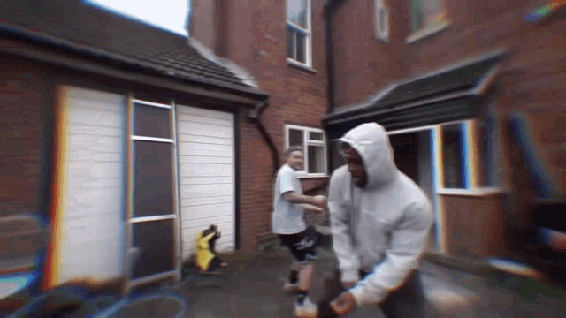 a man in a white hoodie is standing in front of a brick building
