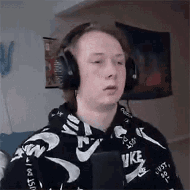 a young man wearing headphones and a nike sweatshirt is looking at the camera .