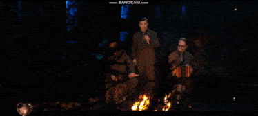 a man singing into a microphone next to a man playing an accordion in front of a fire