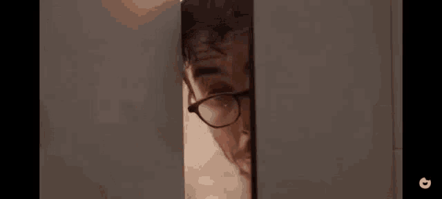 a man wearing glasses and a beard is peeking out of a doorway .