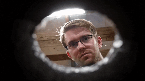 a man wearing glasses is looking through a hole in the wall