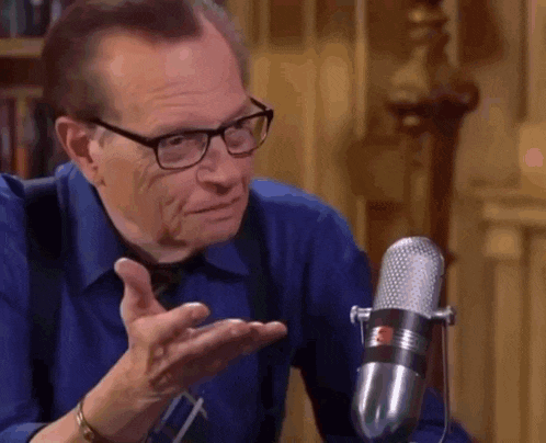 a man wearing glasses is sitting in front of a microphone .