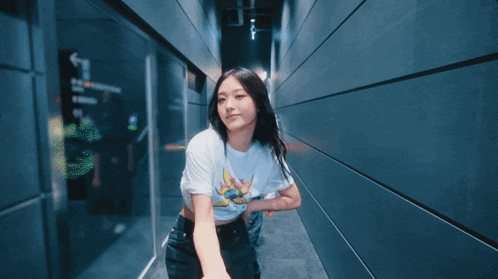 a woman wearing a white t-shirt with a yellow flower on it stands in a hallway