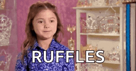 a little girl in a blue shirt is standing in front of a shelf with the word ruffles written on it .