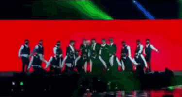 a group of men in suits are dancing on a stage in front of a red background .