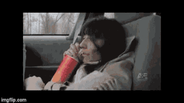 a woman is sitting in the back seat of a car drinking a soda