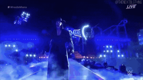 a man in a black hat is walking on a stage with a sign that says emania on it