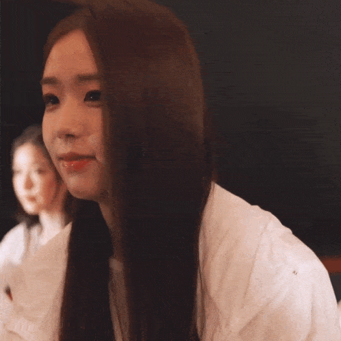 a woman with long brown hair wearing a white shirt looks at the camera