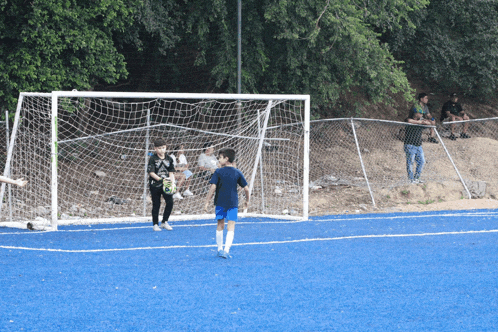 a boy in a blue shirt with the word soccer on it runs towards a soccer goal