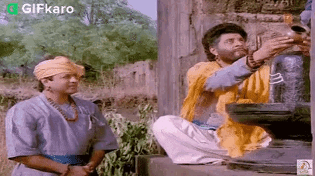 two men are sitting next to each other in front of a stone wall .