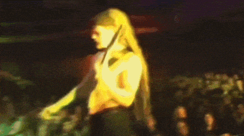 a woman with long blonde hair stands in front of a crowd at a concert with a sign that says i am