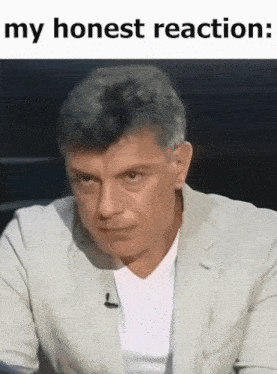 a man in a suit and white shirt is sitting in front of a microphone with the caption my honest reaction .