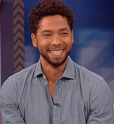 a man with curly hair and a beard is smiling and wearing a denim shirt