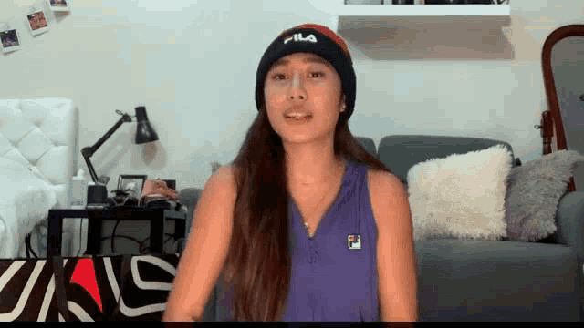 a woman wearing a purple fila tank top and a black fila hat