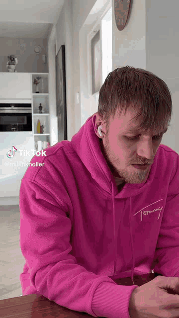 a man wearing a pink tommy hilfiger hoodie is looking at his phone