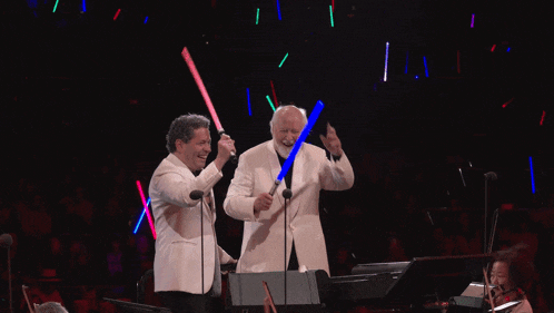 two men are holding lightsabers in front of microphones in a dark room