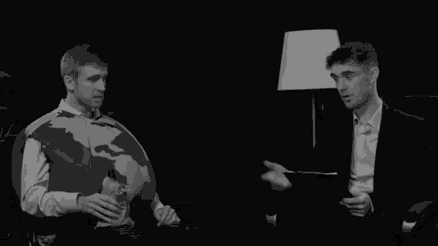 a man in a sweater with a globe on it is talking to another man