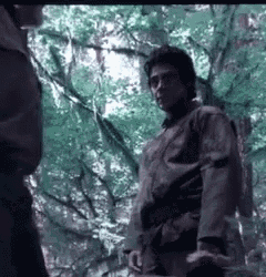 a man in a karate uniform is standing in a forest talking to another man .