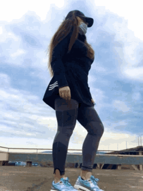 a woman wearing a mask and a black hat stands on a bridge