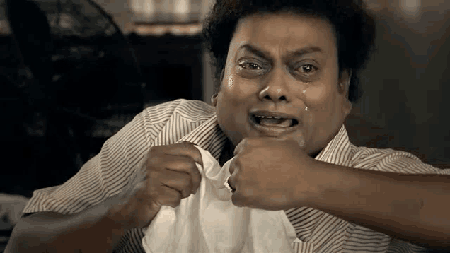 a man in a striped shirt is crying while holding a towel over his mouth .
