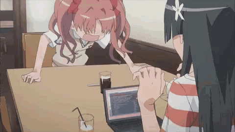 two anime girls are sitting at a table with a laptop and a drink