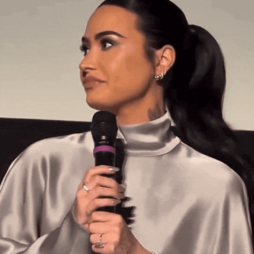 a woman is holding a microphone while wearing a silver top