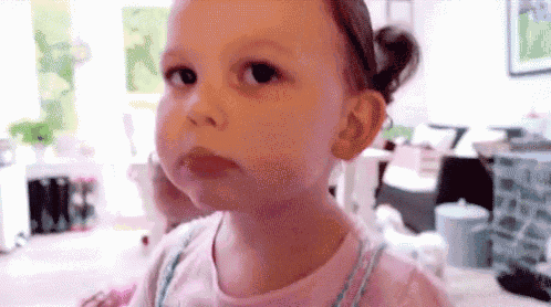 a little girl in a pink shirt is making a funny face while looking at the camera .