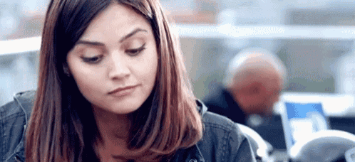 a woman is sitting at a table with a laptop in front of her and looking down .