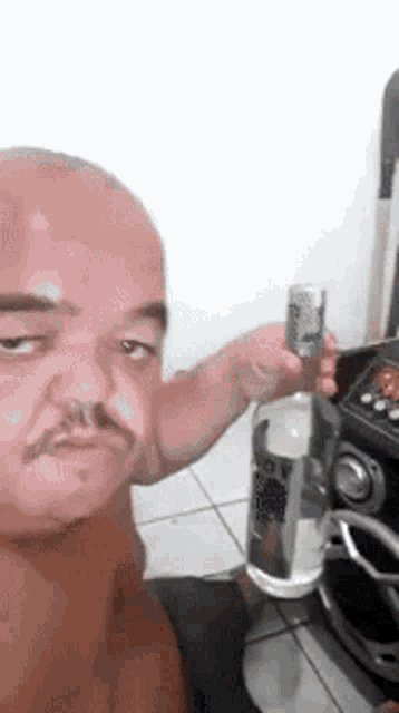 a bald man with a mustache is holding a bottle of vodka in front of a speaker .